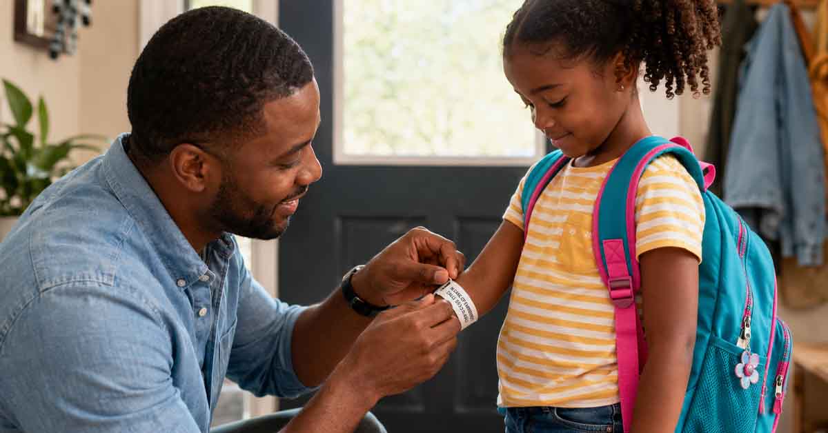 African American parent places an emergency contact bracelet on a child before leaving home.